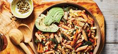 a wooden platter filled with pasta and vegetables next to a bowl of avocado