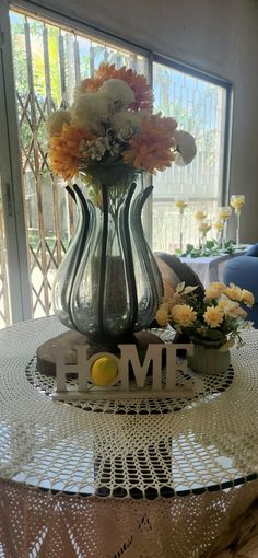 a vase with flowers sitting on top of a table next to a sign that says home