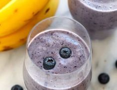 two glasses filled with blueberry smoothie next to bananas