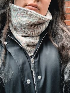 a woman wearing a black leather jacket and a gray knitted neck scarf over her face