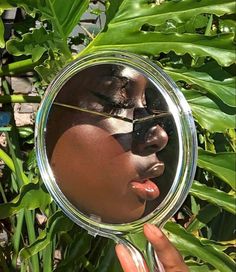 a woman's face is reflected in a round mirror with leaves surrounding her and behind her