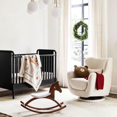 a baby's room with a rocking horse, crib and christmas wreath on the window sill