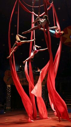 three women performing aerial acrobatic tricks on a circus ring in the dark