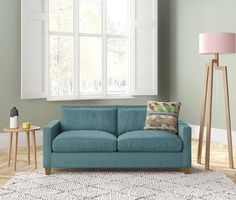 a blue couch sitting in front of a window next to a table with a lamp on it