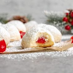 powdered sugar covered pastries are sitting on a wooden board with holly and pine cones in the background