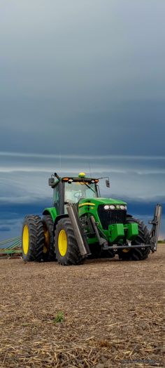 a green tractor is parked in the middle of a field with dark clouds above it