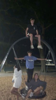 four people are hanging upside down in the grass at night, and one person is standing on a swing set