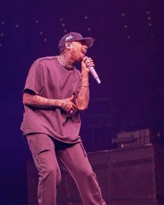 a man standing on top of a stage with a microphone in his hand and wearing a hat