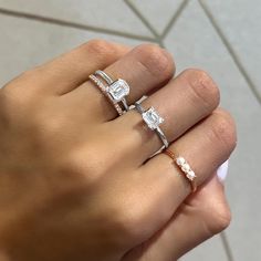 a woman's hand holding two rings with diamonds and pearls on the ring finger