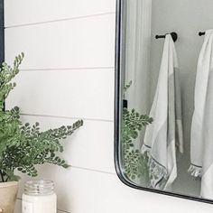 a bathroom mirror sitting above a sink next to a potted plant