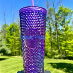 a purple plastic cup sitting on top of a wooden table next to a green field