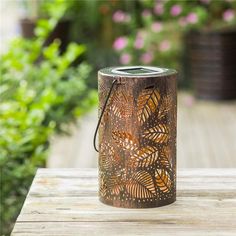 a metal can sitting on top of a wooden table next to some bushes and flowers