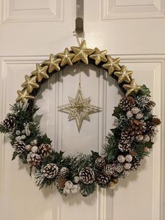 a christmas wreath hanging on a door with gold stars and pineconis around it