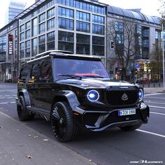 a black mercedes g - class is parked on the side of the road in front of a tall building