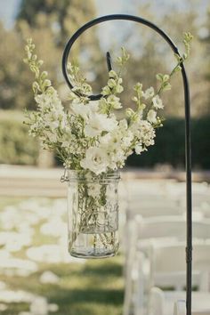 a mason jar with white flowers is hanging from a metal stand at an outdoor ceremony