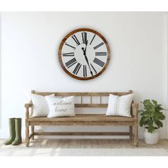 a large clock mounted to the wall above a wooden bench with pillows and boots on it