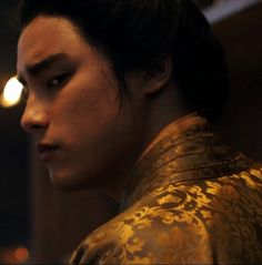 a man with dark hair wearing a gold jacket and looking off into the distance,