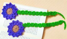 two crocheted flowers sitting on top of an open book next to each other