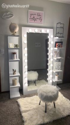 a room with a vanity mirror, stool and lights on it's sides in front of a white bookcase