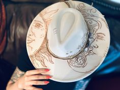 🌙✨ Embrace celestial elegance with our handcrafted light beige wide brim hat, intricately adorned with a mystical moon and sun design and embellished with healing crystals. Each hat is carefully hand burned to create a unique and enchanting piece that exudes mystic energy. 🔮 Our wide brim hat is the perfect accessory to elevate your style while embracing the healing powers of crystals. The combination of the moon and sun motifs symbolizes balance, harmony, and spiritual alignment, making this hat not only a fashion statement but a powerful talisman for your everyday wear. 🌟 Made with high-quality materials and attention to detail, this wide brim hat is a one-of-a-kind piece that will surely turn heads and spark conversations wherever you go. Whether you're a bohemian soul, a lover of as Summer Festival High Crown Hats, Bohemian Cream Sun Hat For Festival, Custom White Festival Hat, Handmade Bohemian Cream Sun Hat, Unique Summer Fedora With Curved Brim, Artisan White Fedora For Festivals, Cream Bohemian Hats For Festival, Bohemian Cream Handmade Sun Hat, Unique Summer Festival Fedora