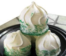 three cupcakes with white frosting and green sprinkles on a black plate