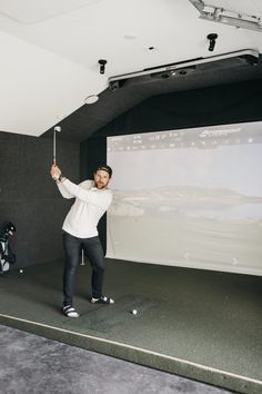 a man holding a golf club in front of a projector screen while standing on top of a carpeted floor