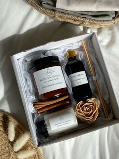 an open box containing two bottles of honey and cinnamon sticks, on top of a bed