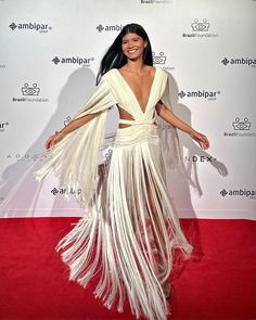 a woman standing on top of a red carpet wearing a white dress with fringes