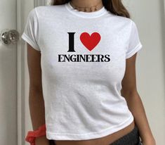 "𝑰 <3 𝑬𝒏𝒈𝒊𝒏𝒆𝒆𝒓𝒔" Soft Tee Engineer your heart's desire with this iconic shirt. At 𝑴𝒚𝑺𝒉𝒊𝒓𝒕𝑺𝒂𝒊𝒅𝑺𝒐, our mission is to inspire love and boost confidence with every shirt we create. 𝑷𝒓𝒐𝒅𝒖𝒄𝒕 𝑫𝒆𝒕𝒂𝒊𝒍𝒔: * 100% cotton * Semi-fitted * Runs true to standard size * Gildan 64000L → Pro Tip: size down for that extra cropped baby tee fit! 𝑪𝒂𝒓𝒆 𝑰𝒏𝒕𝒓𝒖𝒄𝒕𝒊𝒐𝒏𝒔: * Cold machine wash with like colours * Do not bleach * Do not tumble dry * Cool iron on reverse side * D Fitted T-shirt With Heart Graphic For Streetwear, Trendy Cotton T-shirt For Valentine's Day, Fitted Casual T-shirt With Heart Graphic, Trendy Crew Neck Top With Heart Graphic, Trendy Valentine's Day T-shirt, Casual Tops With Valentine's Day Graphic Print, Casual Tops With Graphic Print For Valentine's Day, Casual Graphic Print Tops For Valentine's Day, Trendy Graphic Print Tops For Valentine's Day