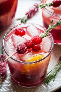 two glasses filled with ice and cranberries on top of a table next to other drinks