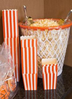 orange and white striped popcorn bags in front of a basket with spoons next to it