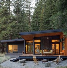 a small cabin in the middle of a forest with chairs and tables on the ground