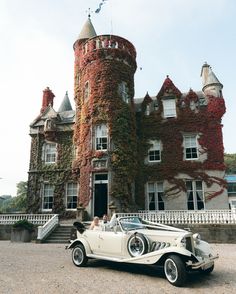 an old car parked in front of a large building with ivy growing on it's walls