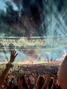 a large crowd at a concert with their hands in the air and lights shining down on them