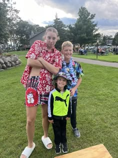 two children and an adult posing for a photo in front of a picnic table on the grass