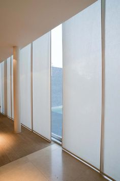 an empty room with white vertical blinds on the wall and floor, in front of a large window