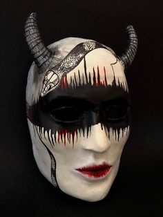 a white mask with black and red designs on it's face, including horns