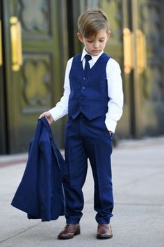 a young boy in a blue suit and tie is holding a jacket on the sidewalk