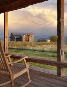 a wooden rocking chair sitting on top of a porch next to a field and barn