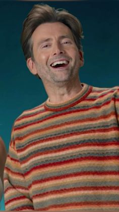 a man laughing while wearing a striped sweater