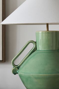 a green vase sitting on top of a table next to a white lampshade