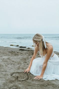 a woman sitting in the sand on top of a beach