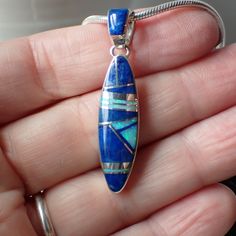 This stunning sterling silver pendant is created and stamped by Navajo artist Cathy Webster. It features an inlay design of Lapis Lazuli, blue opal with sterling silver. The pendant measures 1.6" long including the bail by .4" wide. The interior dimension of the bail is 4.3mm. This pendant is photographed on a 1.8mm snake chain which comes in your choice of 16, 18, 20 or 24 inches. We default to 18", Please leave a note with your order if you prefer a different length. Blue Sterling Silver Necklace With Inlay, Southwestern Blue Necklace With Inlay, Southwestern Blue Inlay Necklace, Southwestern Style Blue Inlay Necklace, Lapis Lazuli Blue, Inlay Design, Spiny Oyster, Blue Opal, Snake Chain