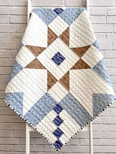 a white chair with a blue and brown quilt hanging on the wall next to a brick wall