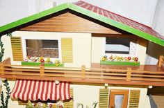 a doll house with green roof and red awnings on the balcony, next to a white wall