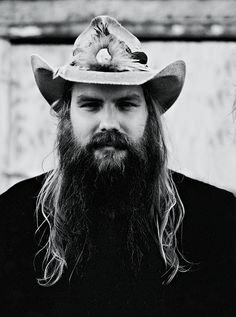 a man with long hair and a beard wearing a hat that has a bird on it