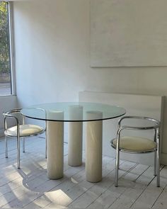 a glass table with two chairs next to it in front of a wall and window