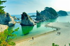 people are walking on the beach next to some rocks and green water in the ocean