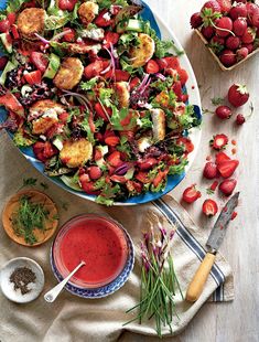 a salad with dressing on the side and strawberries next to it, along with other ingredients