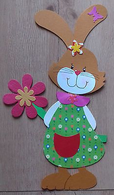 a paper cutout of a bunny holding a flower on a wooden background with pink and green flowers